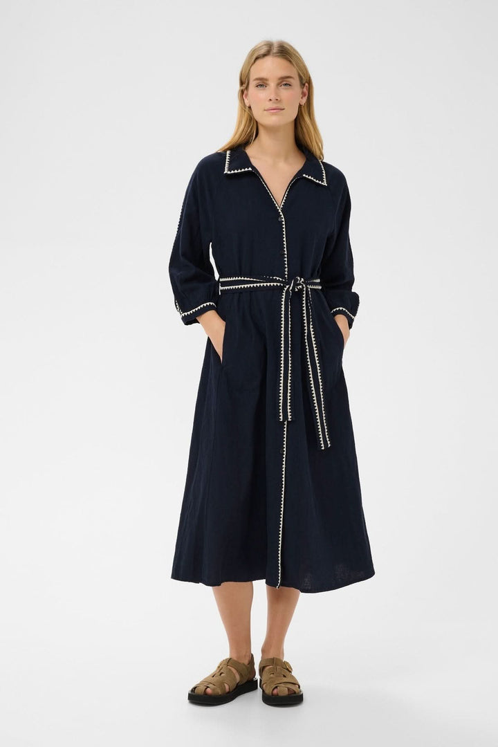 Femme portant une Robe ceinturée Sicillias bleue avec ceinture nouée et manches 3/4, style moderne et fluide.