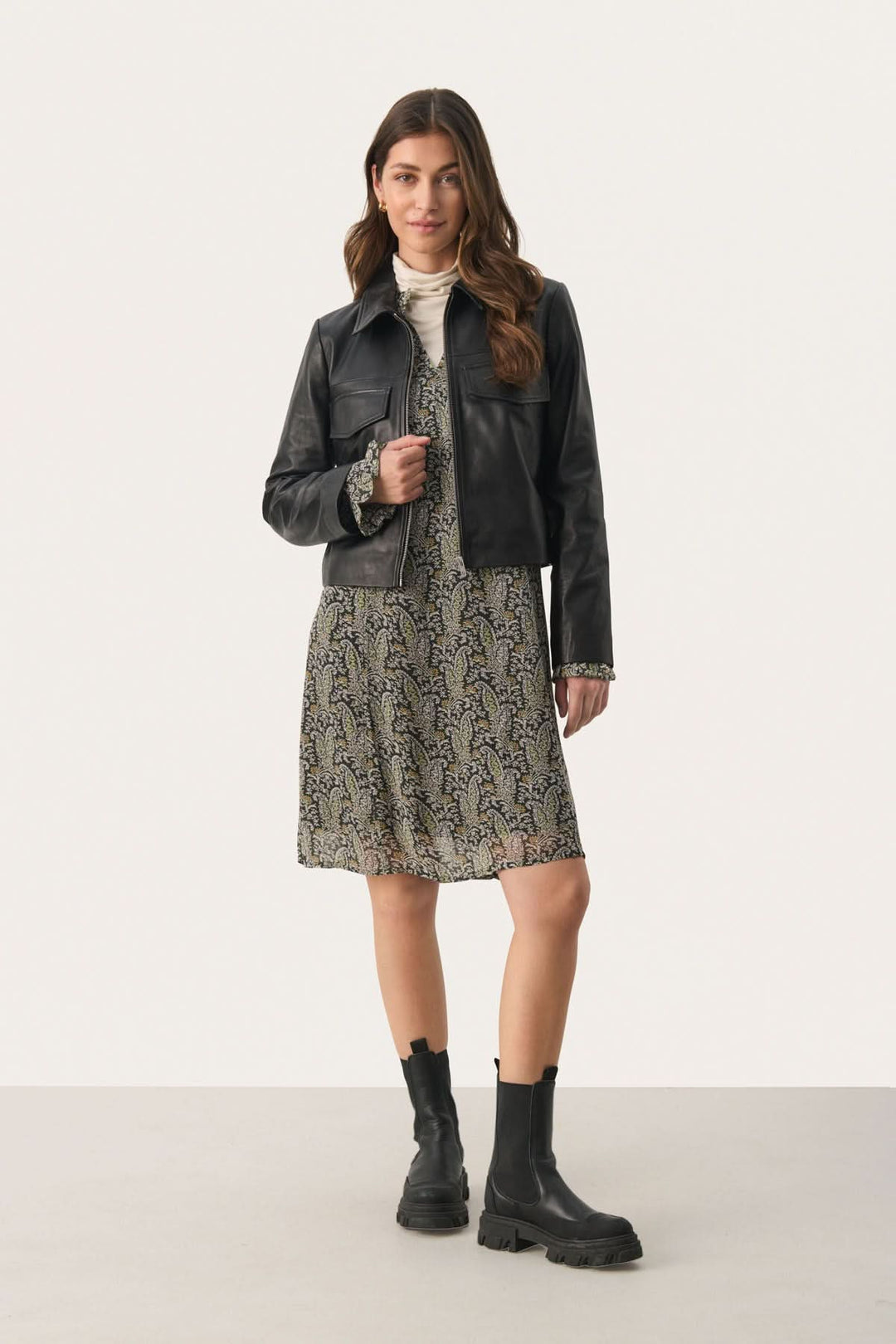 Femme portant une robe courte Botella avec une veste en cuir noir et des bottines, affichant un style élégant.