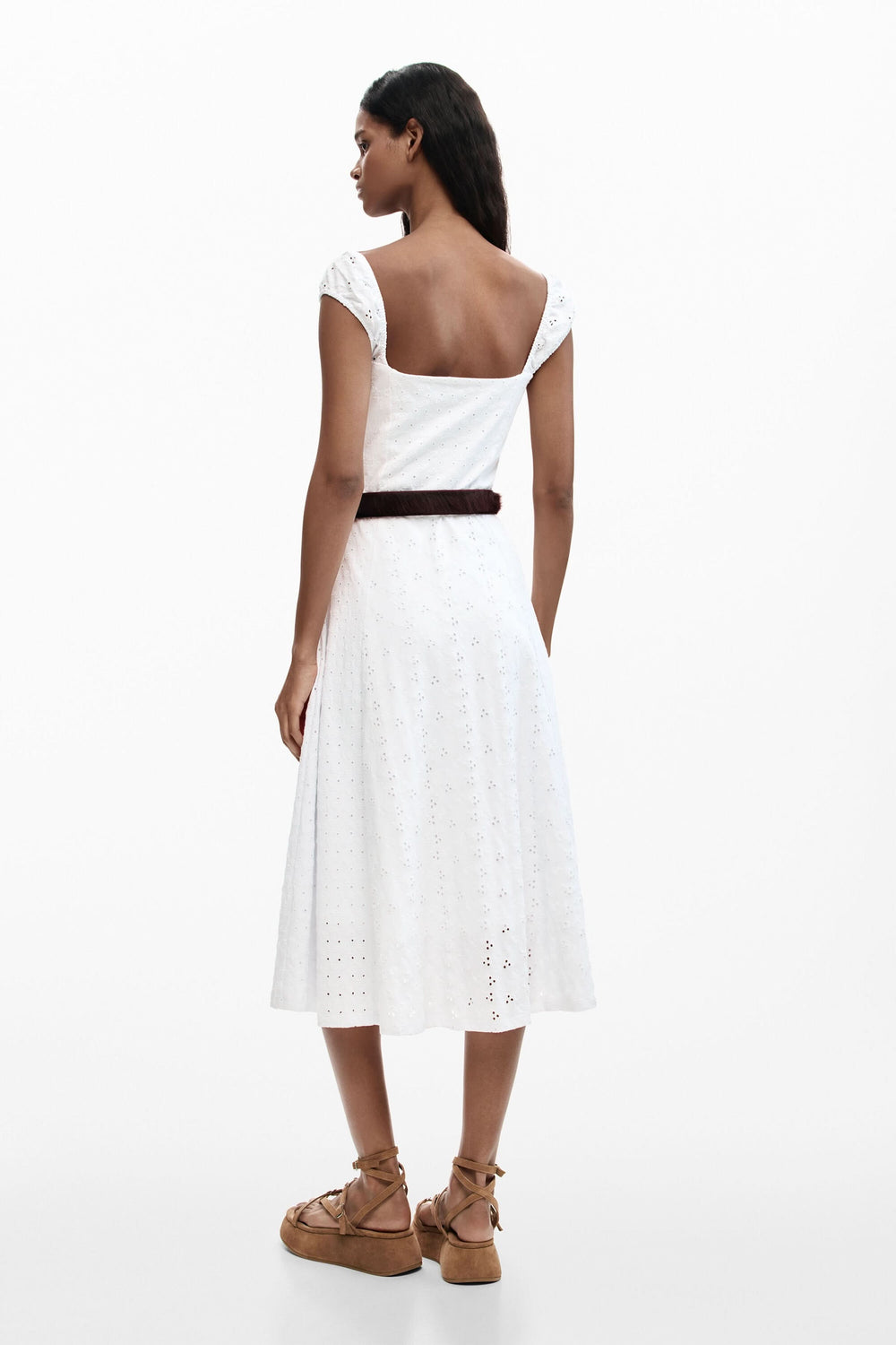 Femme portant une robe midi brodée en broderie anglaise, vue de dos, soulignant l'élégance estivale naturelle du vêtement.