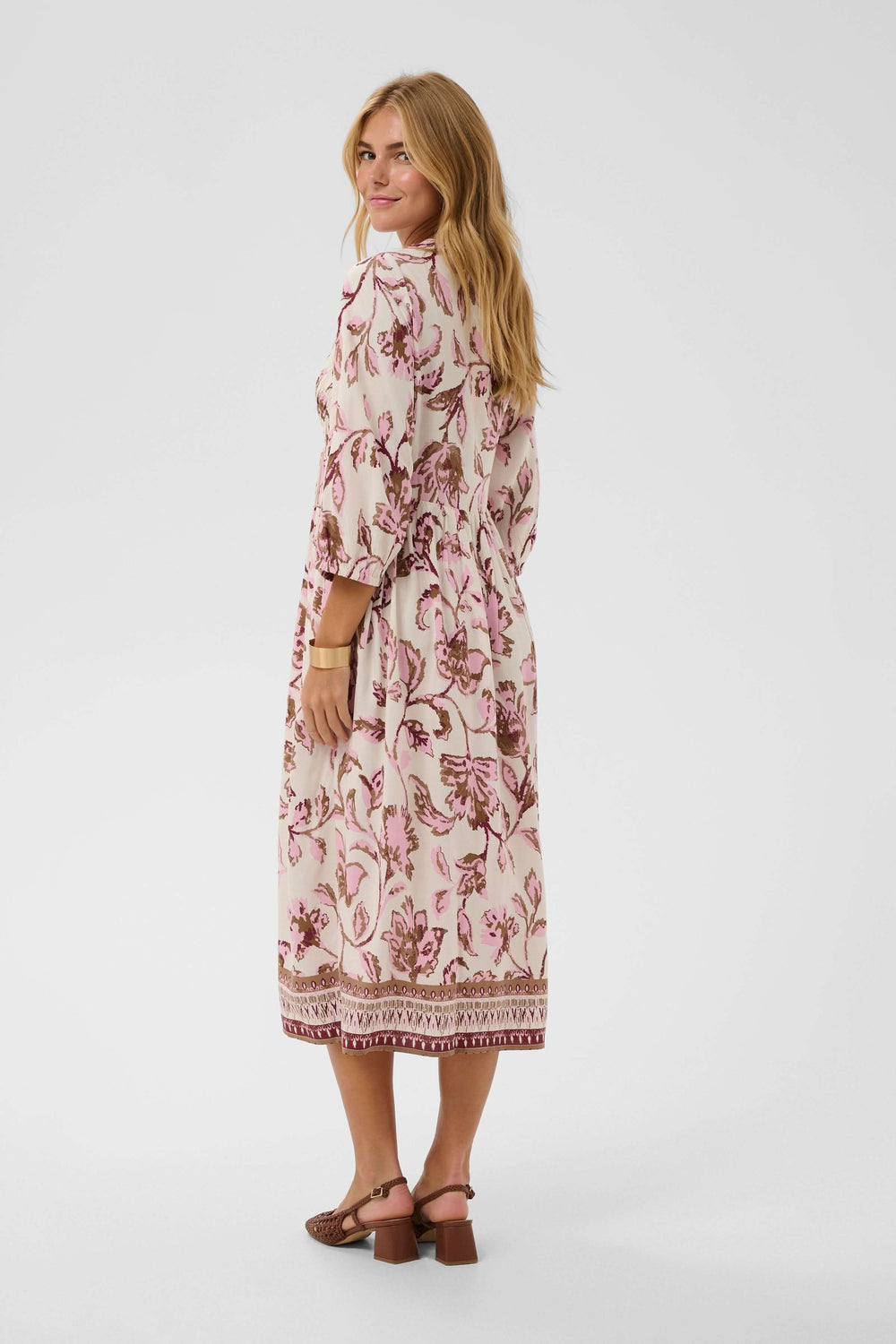 Femme portant une robe midi fluide à imprimé floral avec encolure en V et manches trois-quarts, mettant en valeur la silhouette.