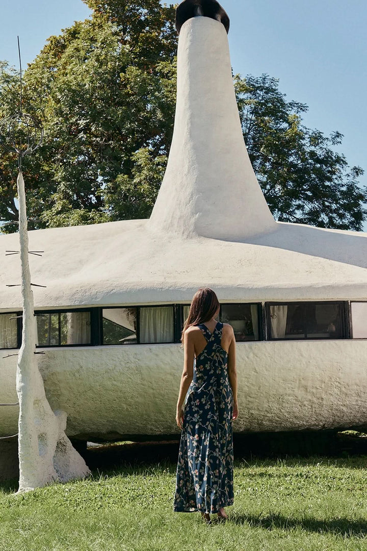 Femme en robe midi sans manches à imprimé floral devant une maison unique en plein air