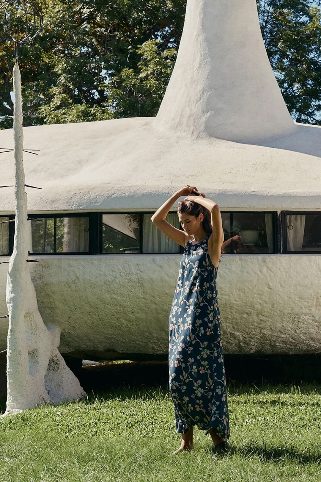Femme portant une robe midi sans manches à imprimé floral devant un bâtiment blanc, style estival et fluide.