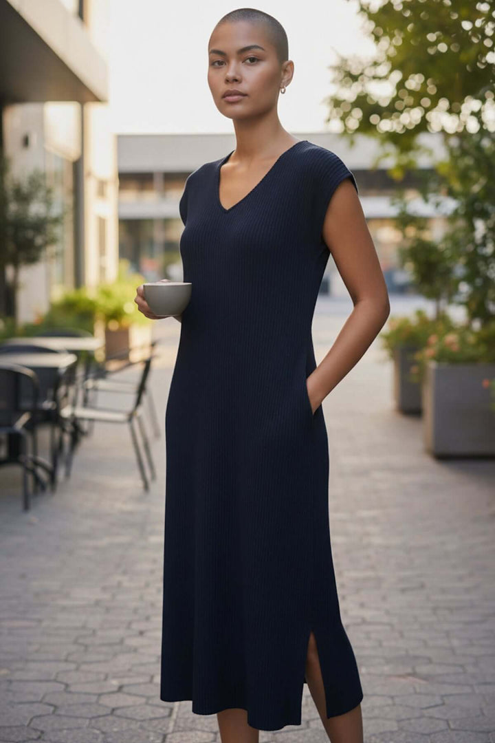 Femme portant une robe plissée avec poches, coupe droite et décolleté en V, dans un cadre urbain élégant.