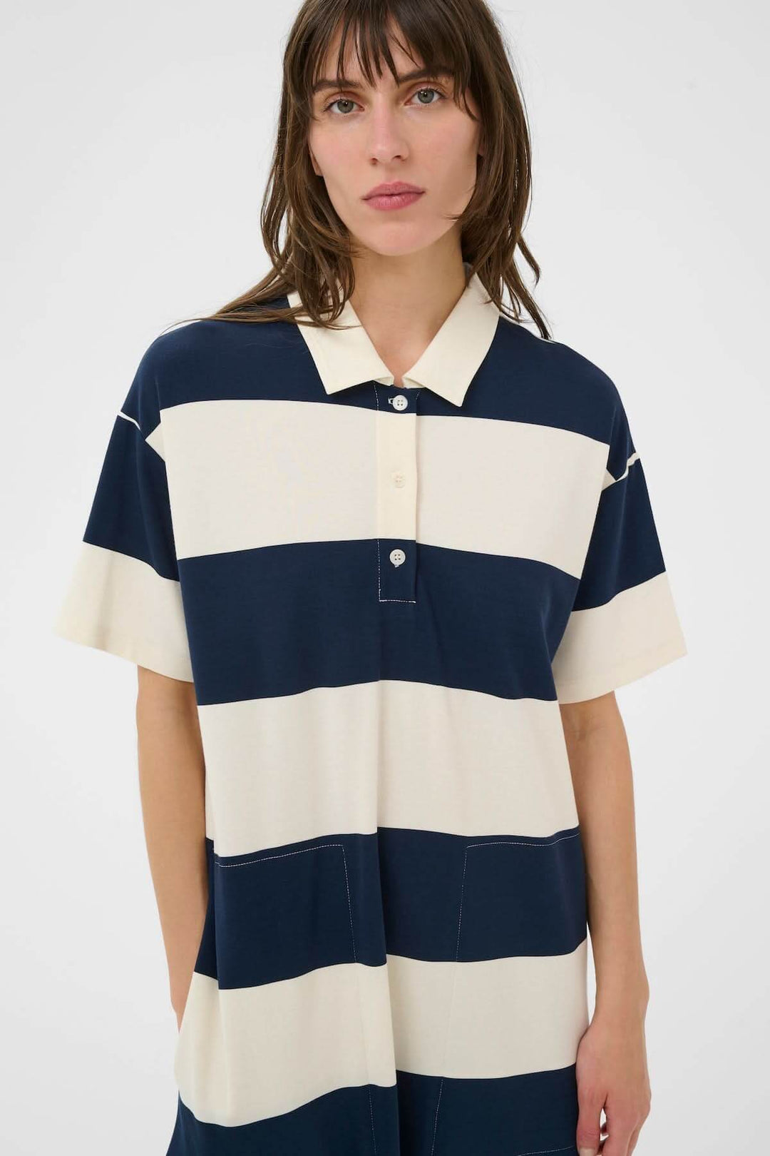Femme portant une robe polo Alise style sport chic avec bandes graphiques pour un look décontracté. Longueur midi, coupe droite, col polo.