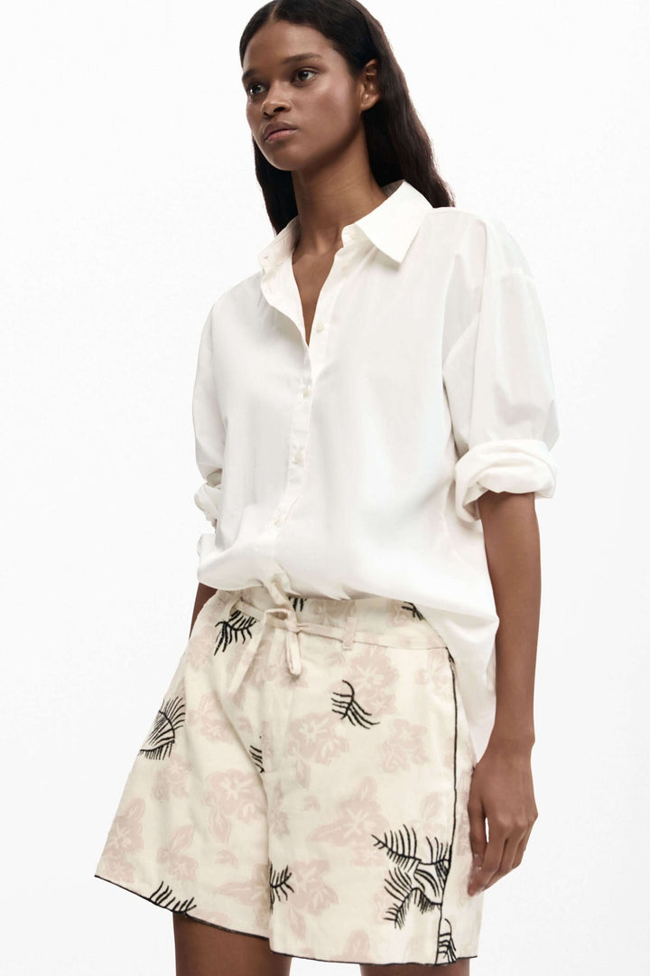 Femme portant un short fluide à imprimé brodé avec motif élégant et poches latérales, idéal pour un look décontracté et raffiné.