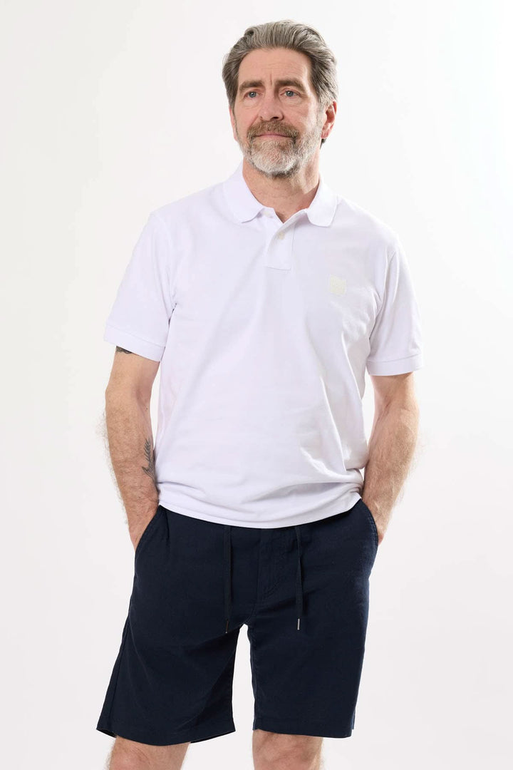 Homme portant un polo blanc et un short à taille élastique, posant avec un look décontracté et élégant.
