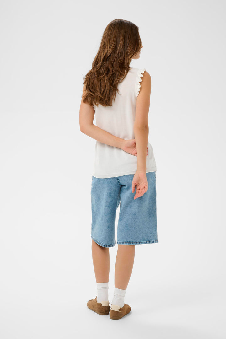 Femme portant un T-shirt Desten sans manches, léger et féminin, avec détails volantés et encolure en V, associé à un jean décontracté.