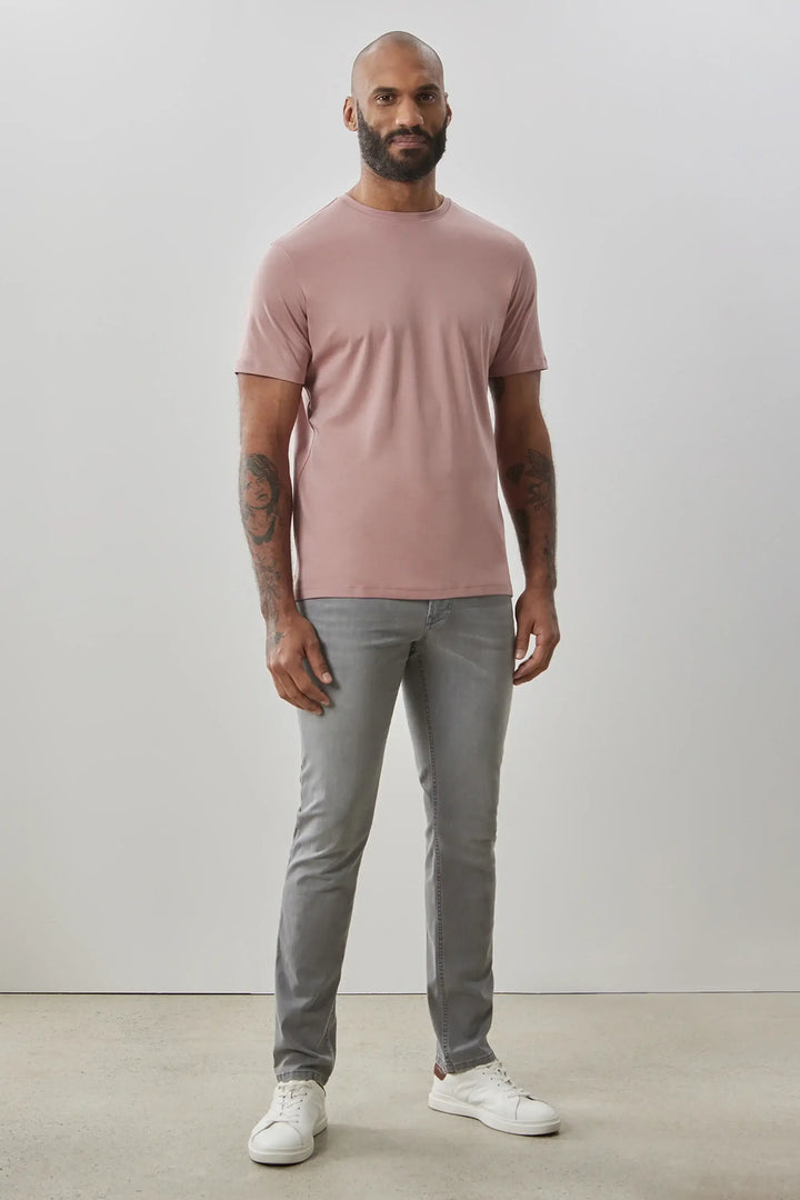 Homme portant un t-shirt rose à manches courtes et un pantalon gris, style minimaliste et moderne.