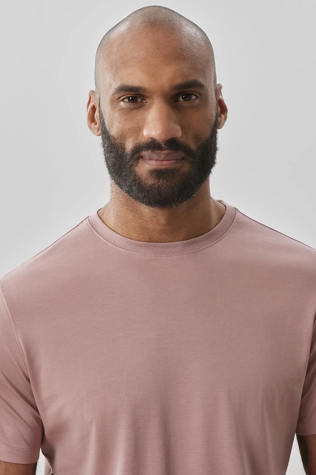 Homme portant un t-shirt à manches courtes rose, style moderne et minimaliste, sur fond neutre.