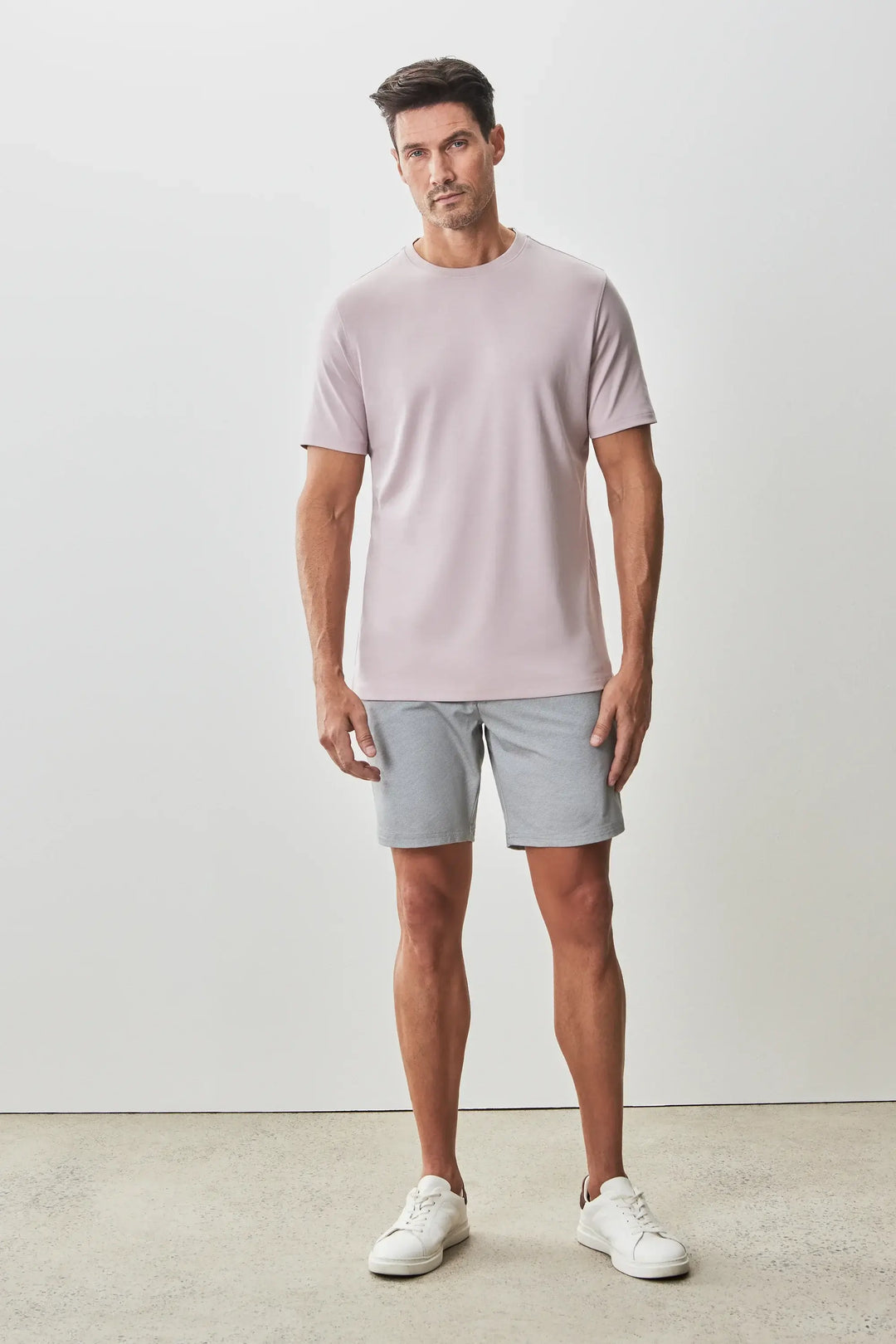 Homme portant un t-shirt Georgia à manches courtes, coloris léger, avec un short gris et des sneakers blanches.