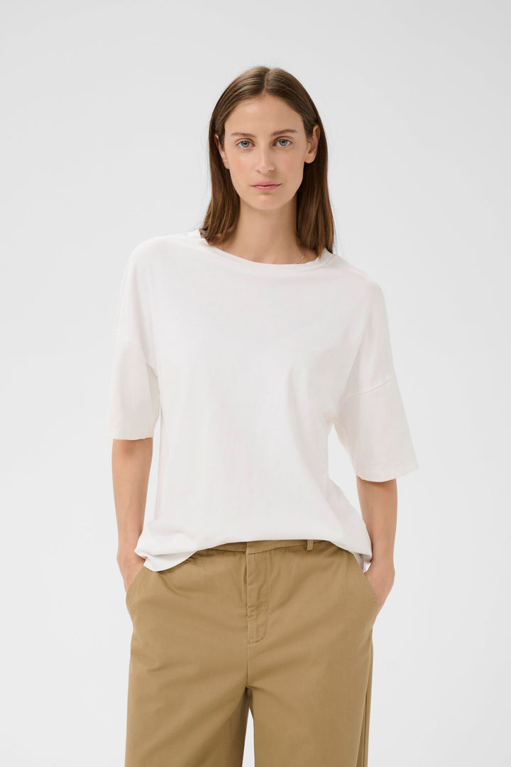Femme portant le T-shirt Sophie fluide à nouer au dos, blanc, manches courtes larges, encolure ronde, coupe ample pour un confort absolu.