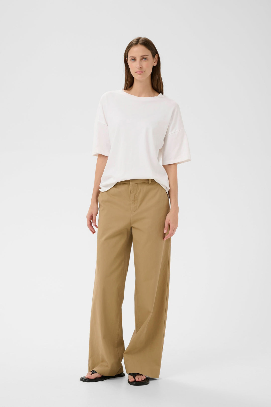 Femme portant un T-shirt Sophie fluide à nouer au dos, ample et élégant, avec un pantalon beige. Description du produit en français.
