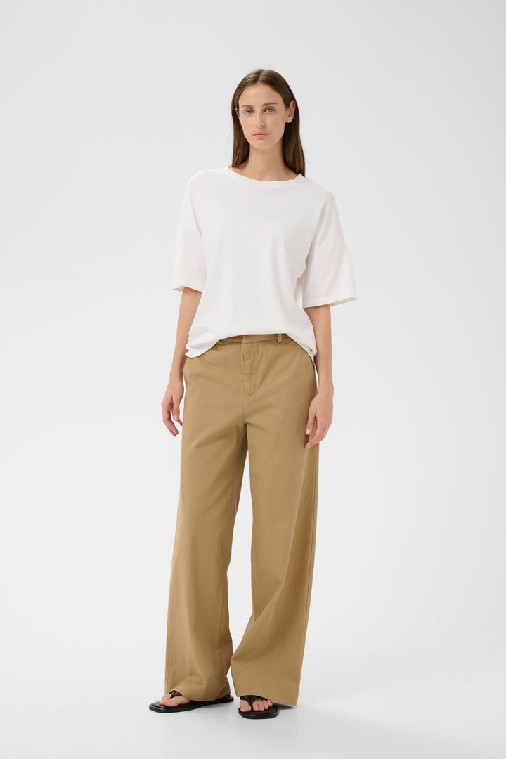 Femme portant un T-shirt Sophie fluide à nouer au dos, ample et élégant, avec un pantalon beige. Description du produit en français.