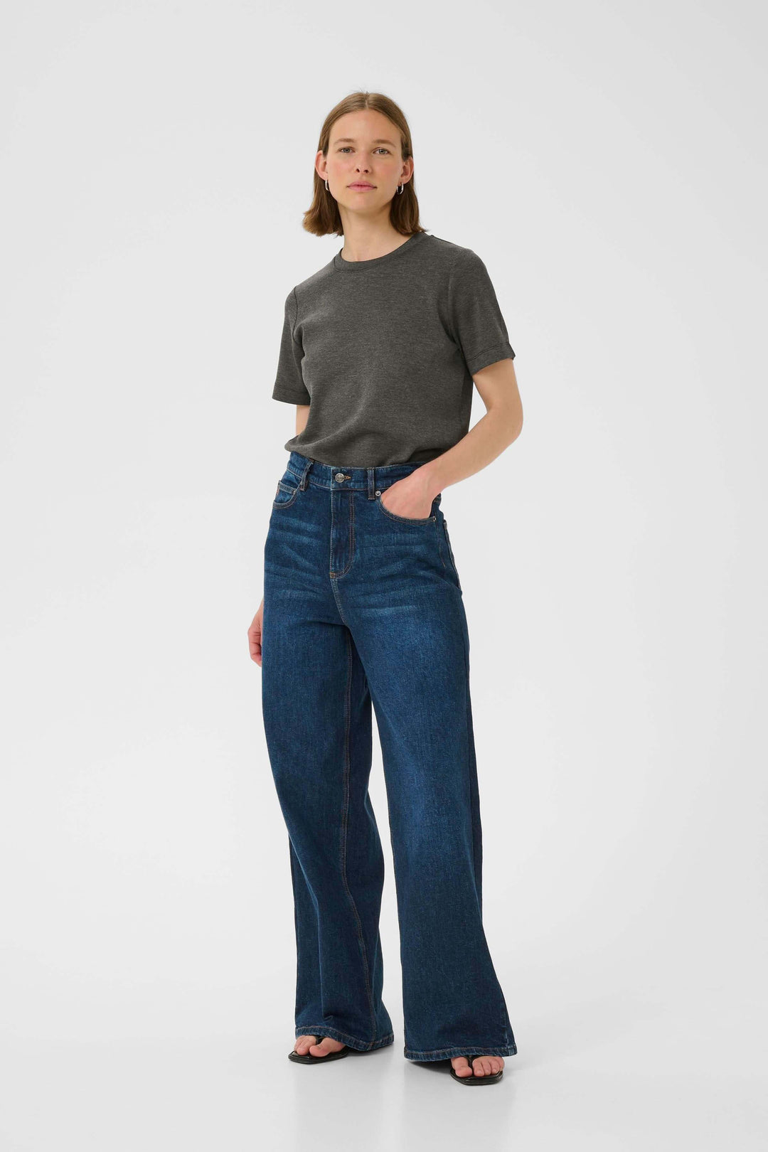 T-shirt minimaliste gris avec jeans évasés, look décontracté et élégant sur fond blanc.