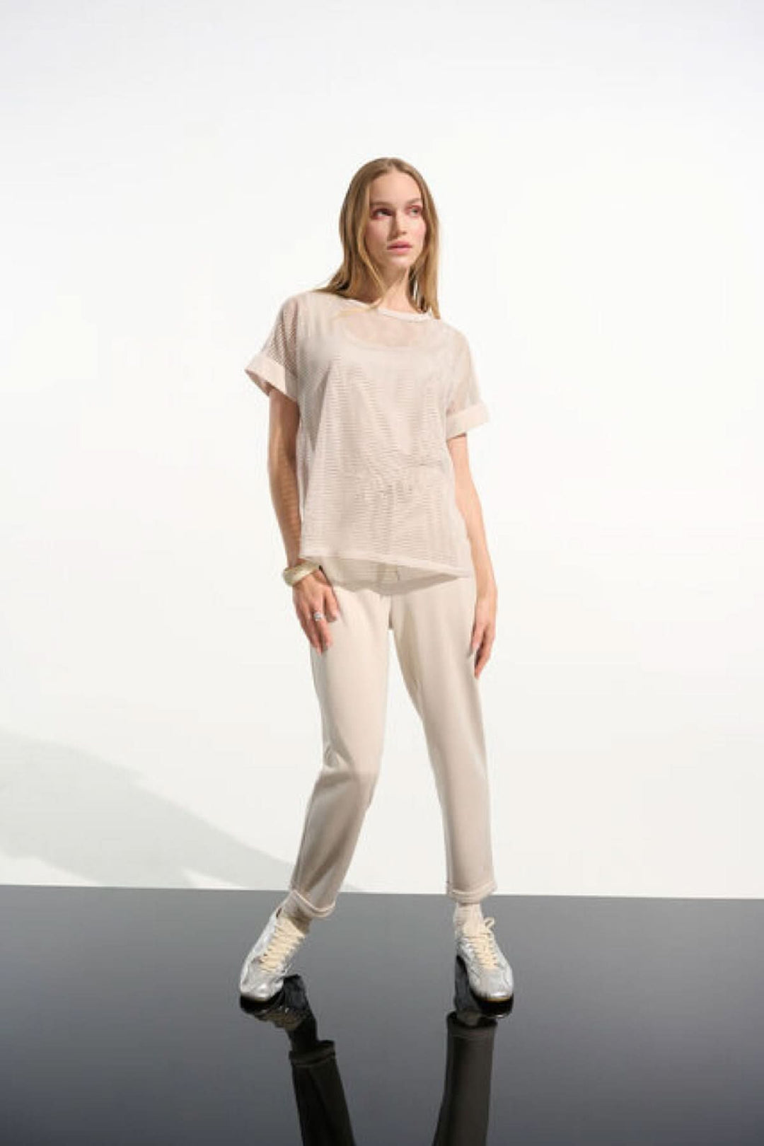 Femme portant un T-shirt ajouré fluide en maille légère avec manches courtes et ourlet droit, style moderne et décontracté.