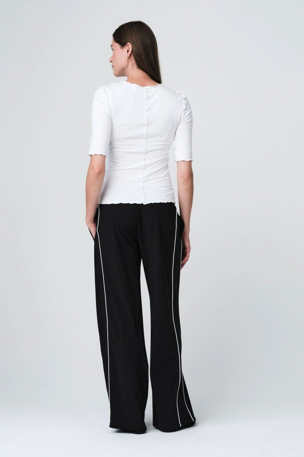 Vue arrière d'une personne portant un T-shirt ajusté à finitions ondulées et un pantalon noir, soulignant une silhouette moderne et épurée.