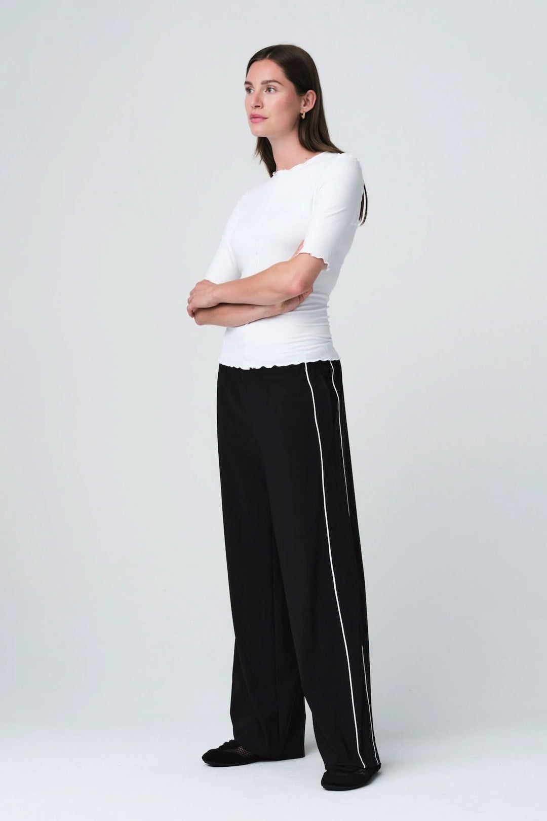 Femme portant un T-shirt ajusté à finitions ondulées, manches courtes, avec pantalon noir, style moderne et épuré.