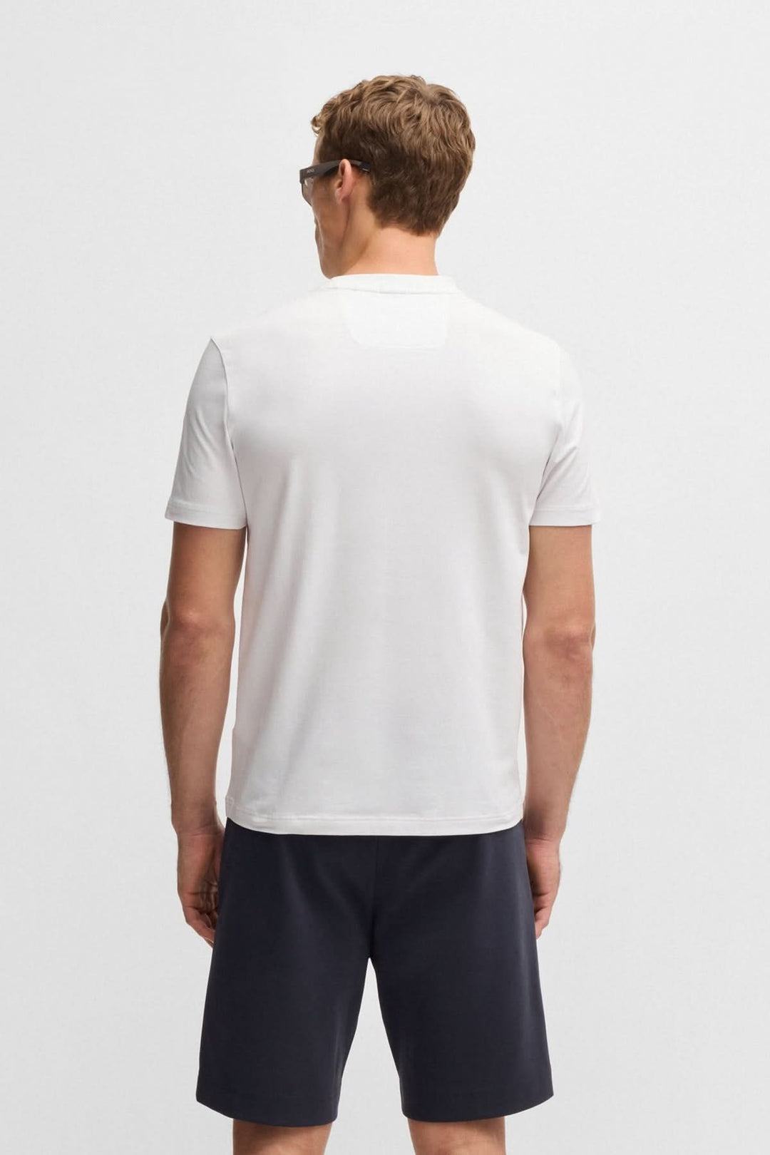 Homme portant un t-shirt blanc à col rond, vue arrière, avec shorts noirs. Style casual moderne.