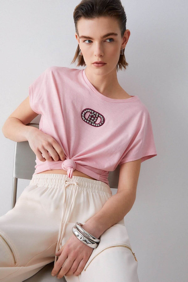 T-shirt avec logo décoratif rose porté par mannequin, manches courtes, encolure ronde, style décontracté. Décris moi le produit.