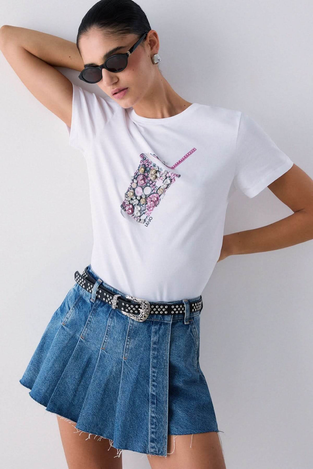 T-shirt avec motif décoratif, manches courtes, porté par modèle avec jupe en jean et lunettes de soleil.