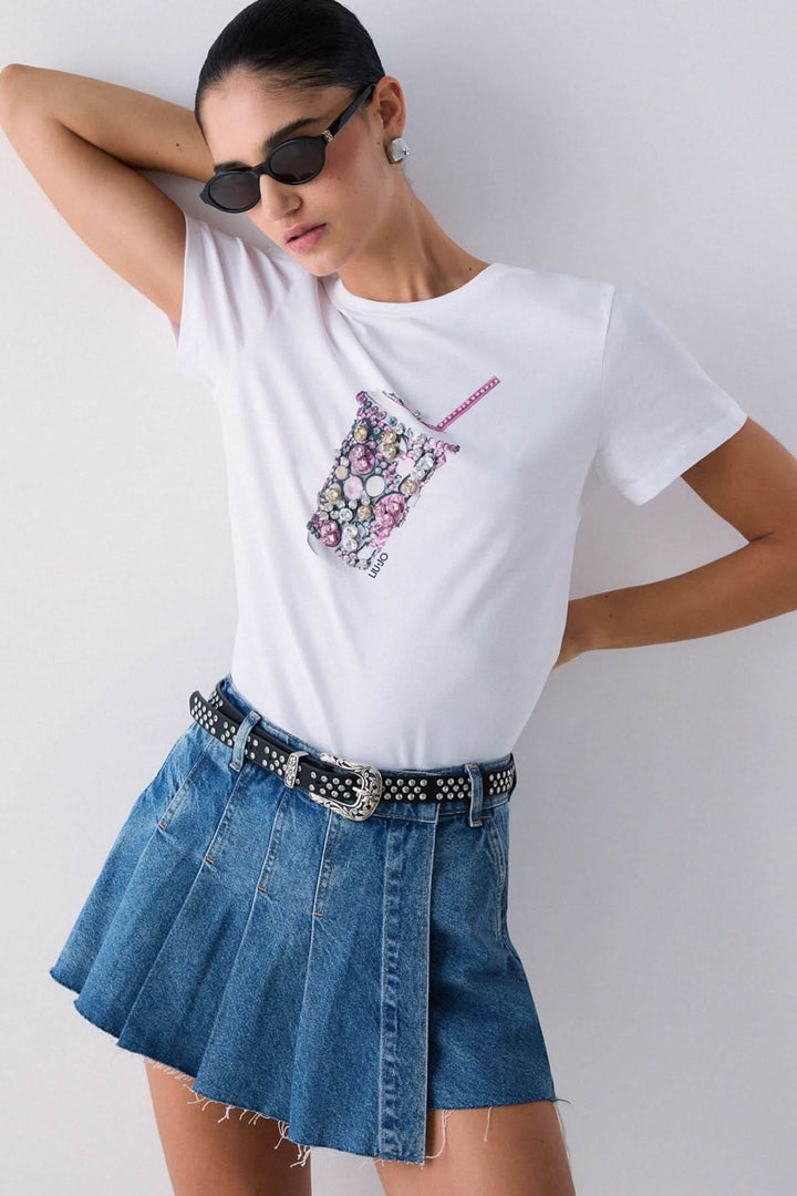 T-shirt avec motif décoratif, manches courtes, porté par modèle avec jupe en jean et lunettes de soleil.