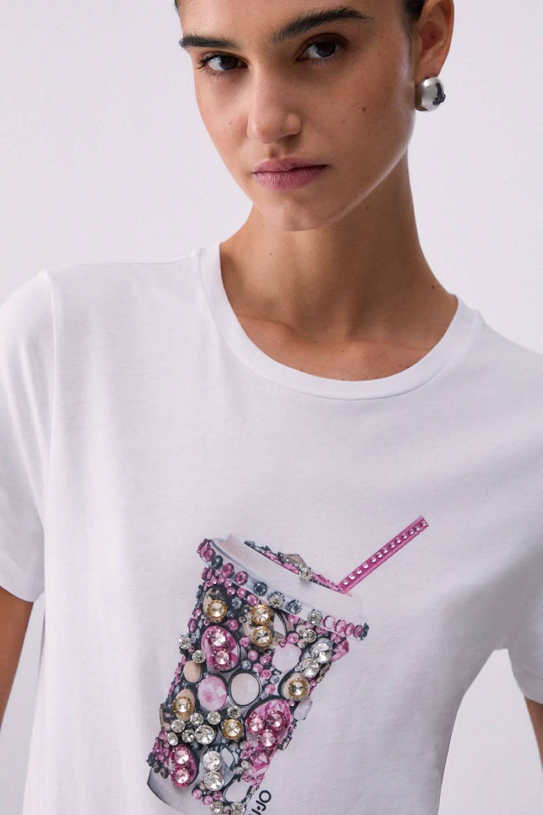 T-shirt avec motif décoratif sur fond blanc, représentant un gobelet orné de bijoux colorés, confortable et élégant pour tenue décontractée.