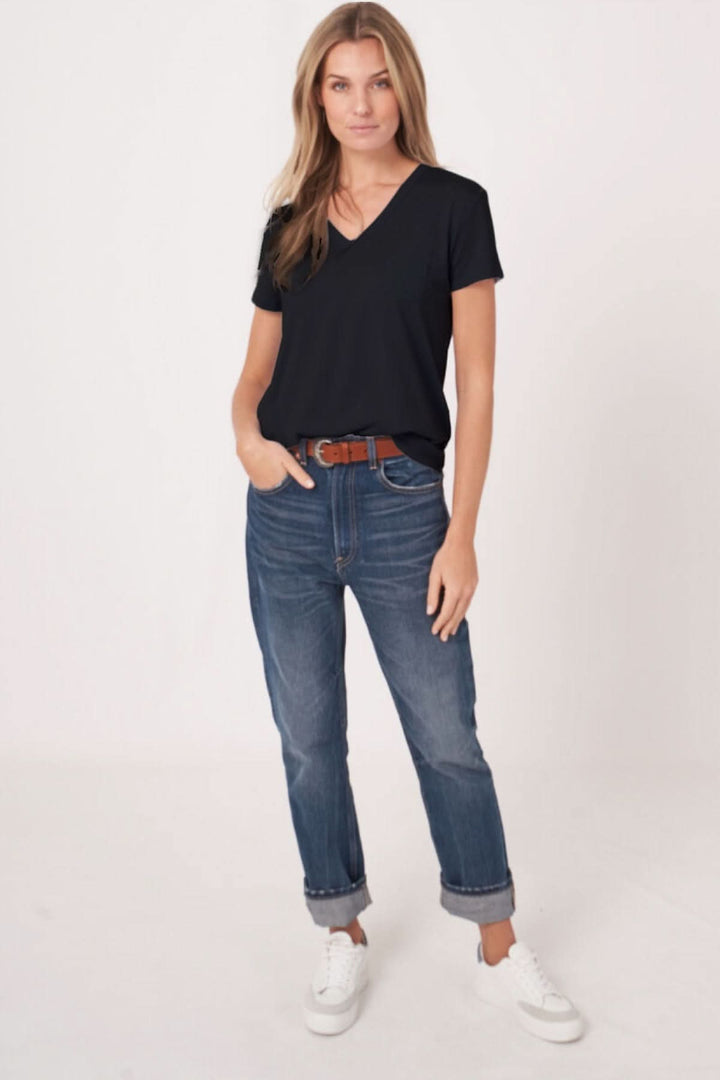 Femme portant un T-shirt col en V manches courtes noir, jeans décontractés, et baskets blanches, style moderne et polyvalent.