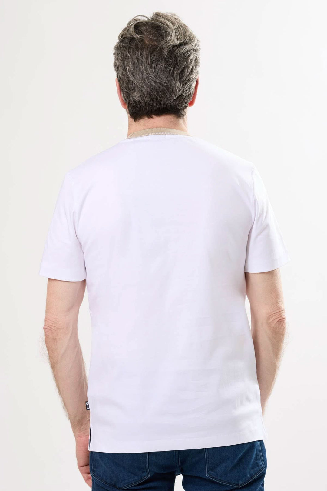 Homme portant un t-shirt blanc minimaliste à col rayé, vue de dos, coupe droite et épurée.