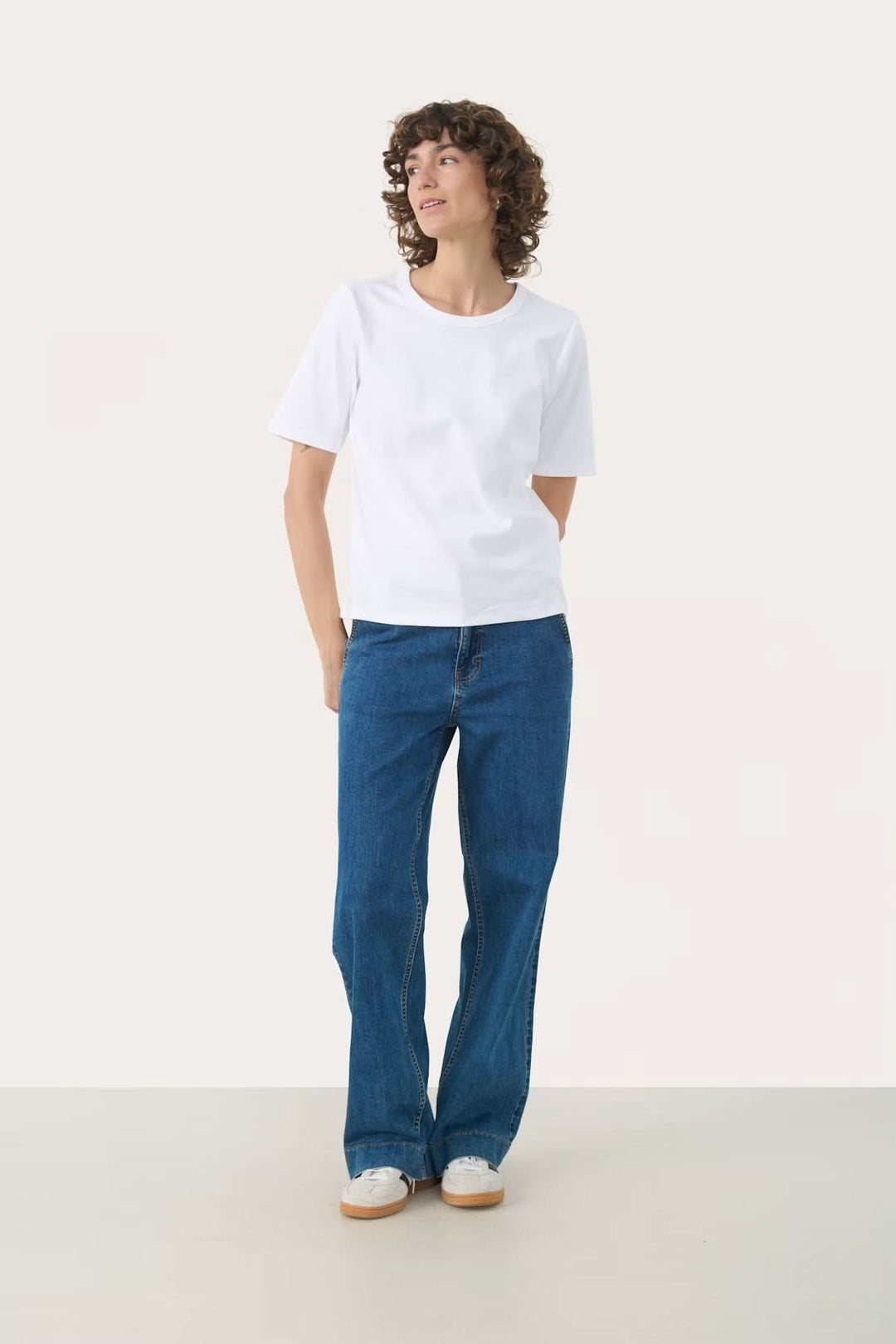 Femme portant un t-shirt blanc à col rond avec un jean bleu, style décontracté et moderne.