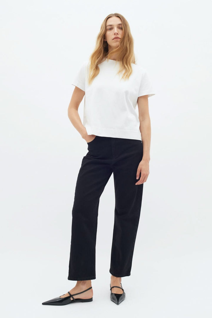 Femme en T-shirt col rond blanc avec pantalon noir, style décontracté et moderne.
