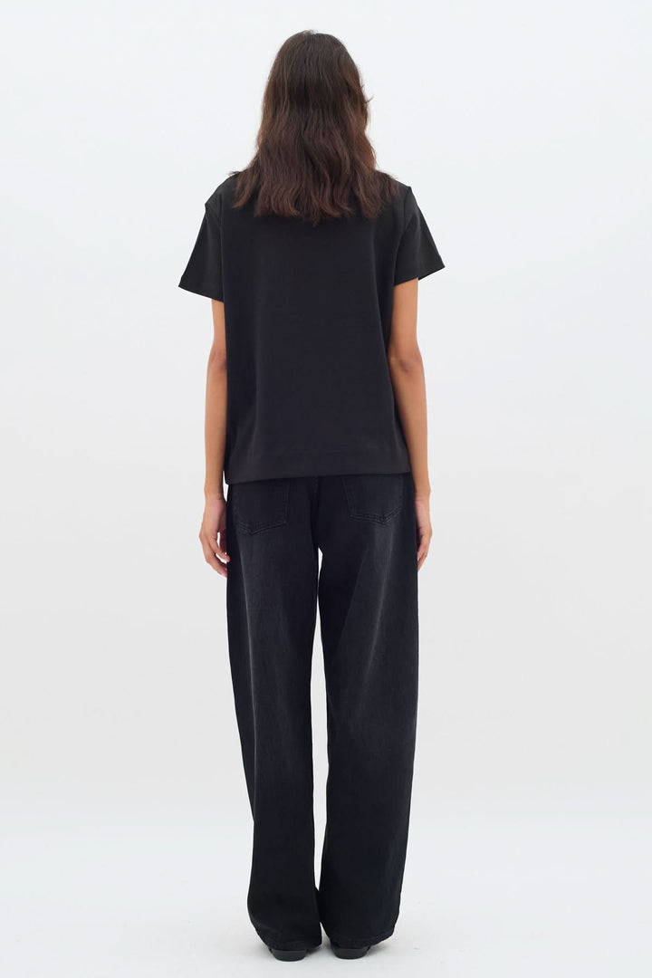 Femme portant un t-shirt noir col rond avec une coupe légèrement ample vue de dos.