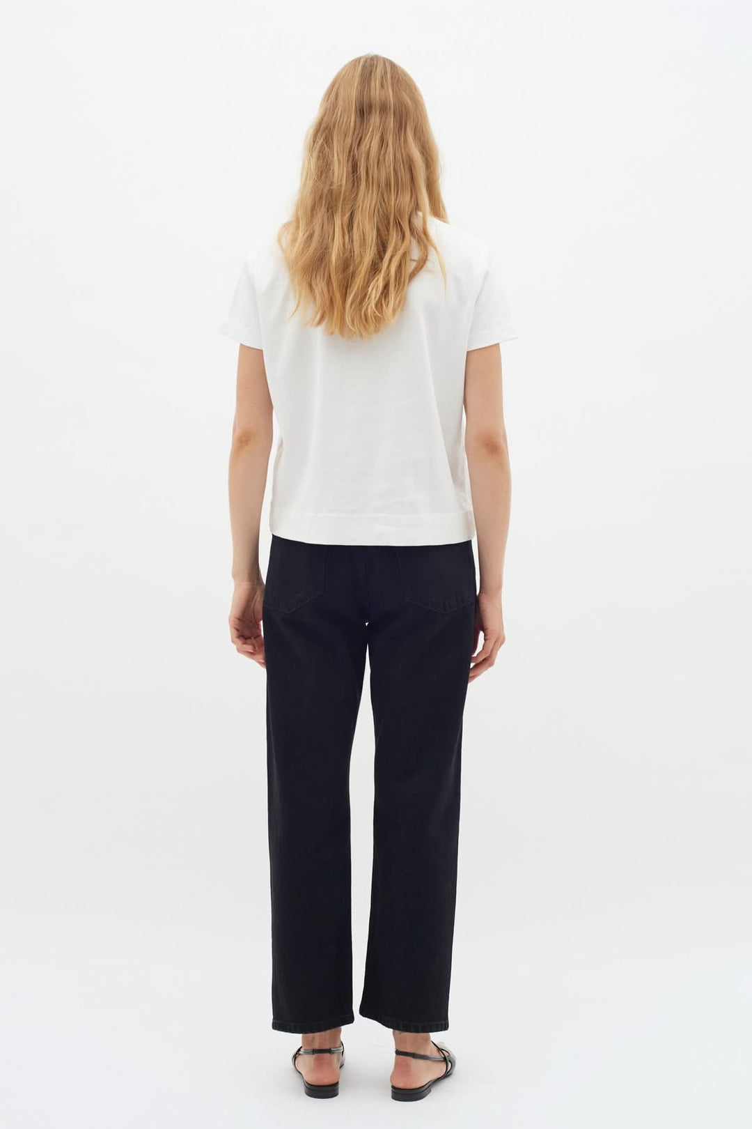 Femme vue de dos portant un T-shirt col rond blanc, associé à un pantalon noir, style décontracté et élégant.