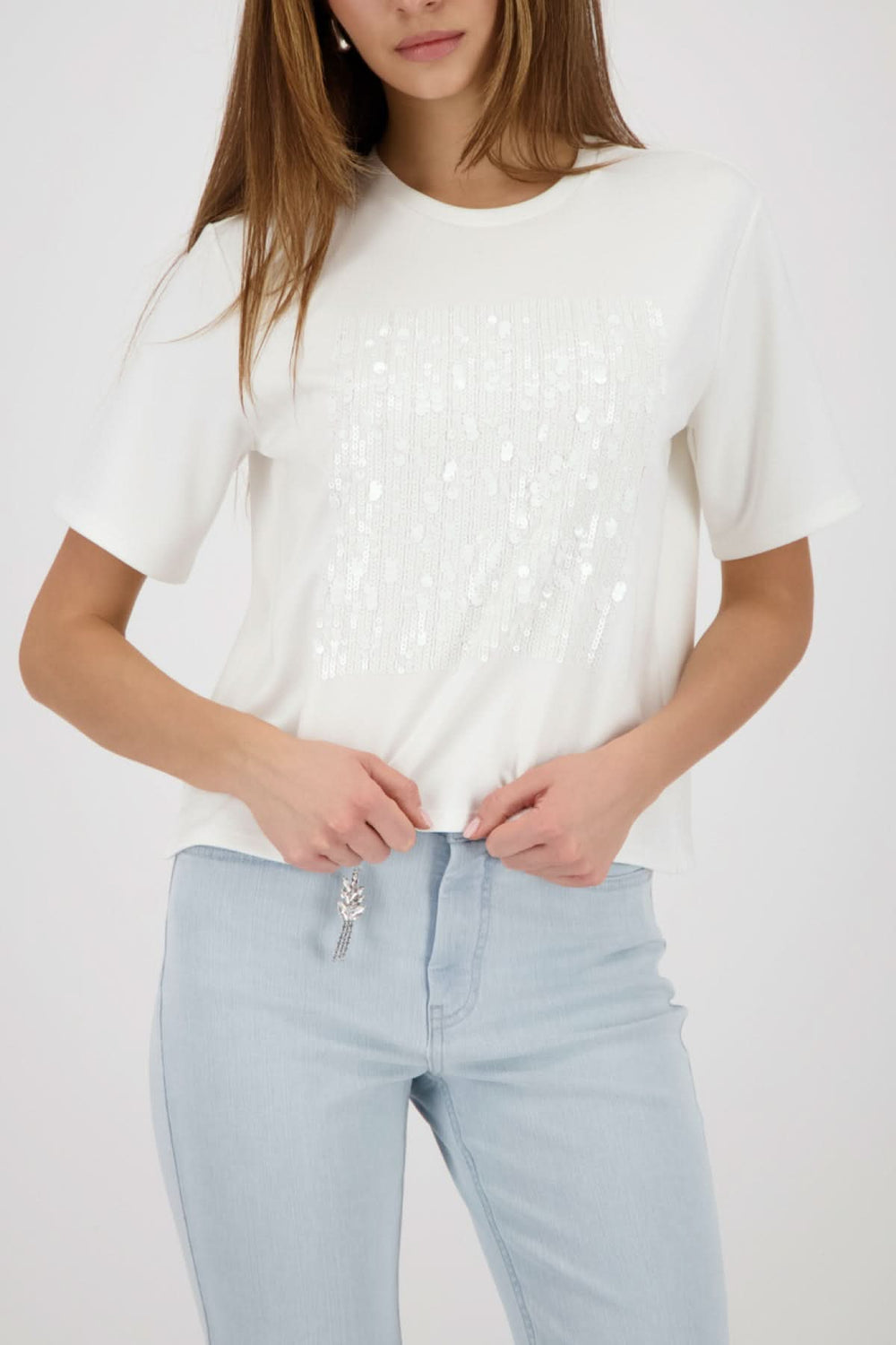Femme portant un t-shirt à empiècement pailleté avec jean clair, coupe droite et manches courtes, silhouette moderne et féminine.