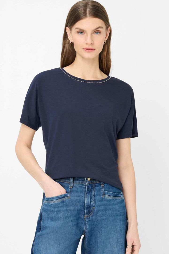 Femme portant un T-shirt encolure perlée Caelen, silhouette fluide et décontractée, manches courtes et détail brillant élégant.