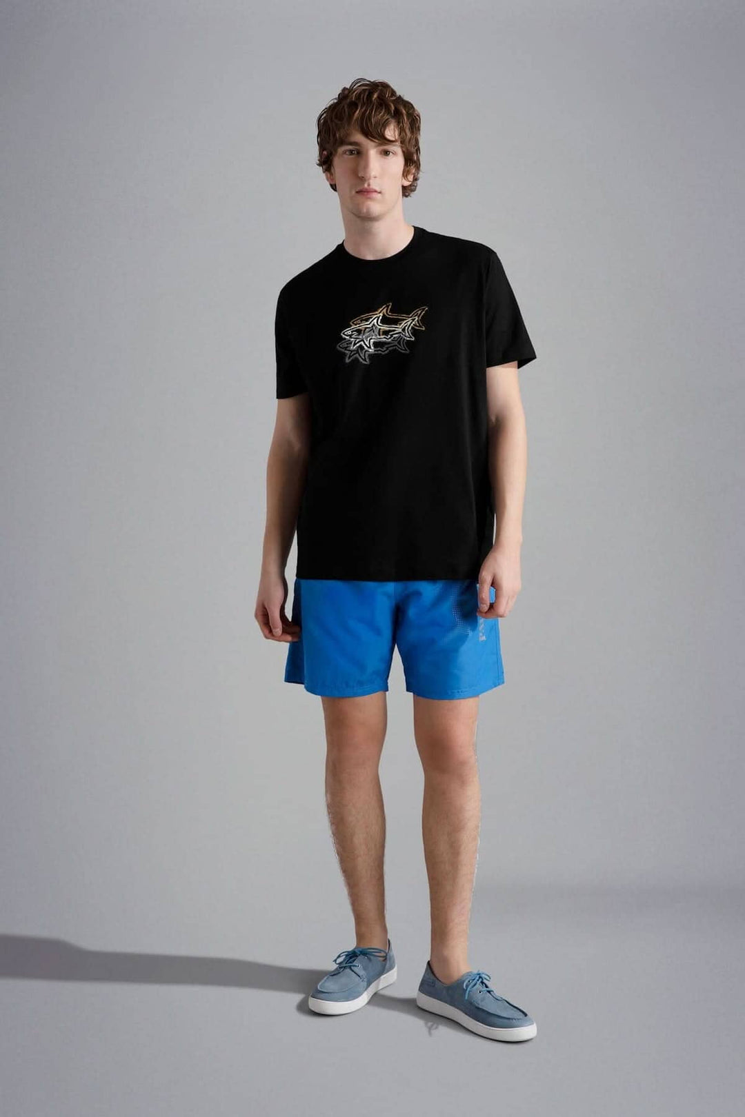 Homme portant un t-shirt noir imprimé 3 requins et un short bleu, look d&