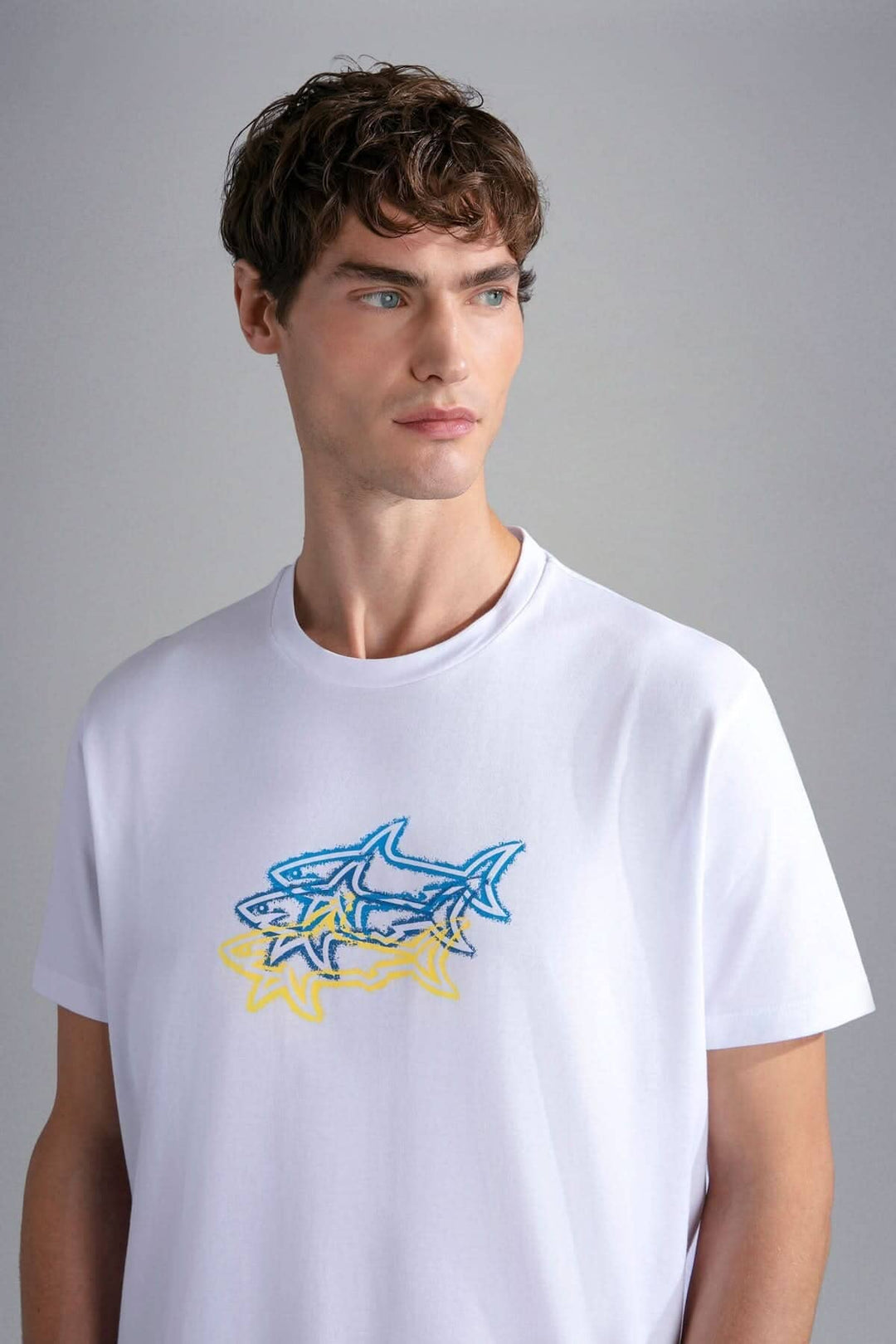 Homme portant un t-shirt blanc avec un design de 3 requins colorés, parfait pour l&