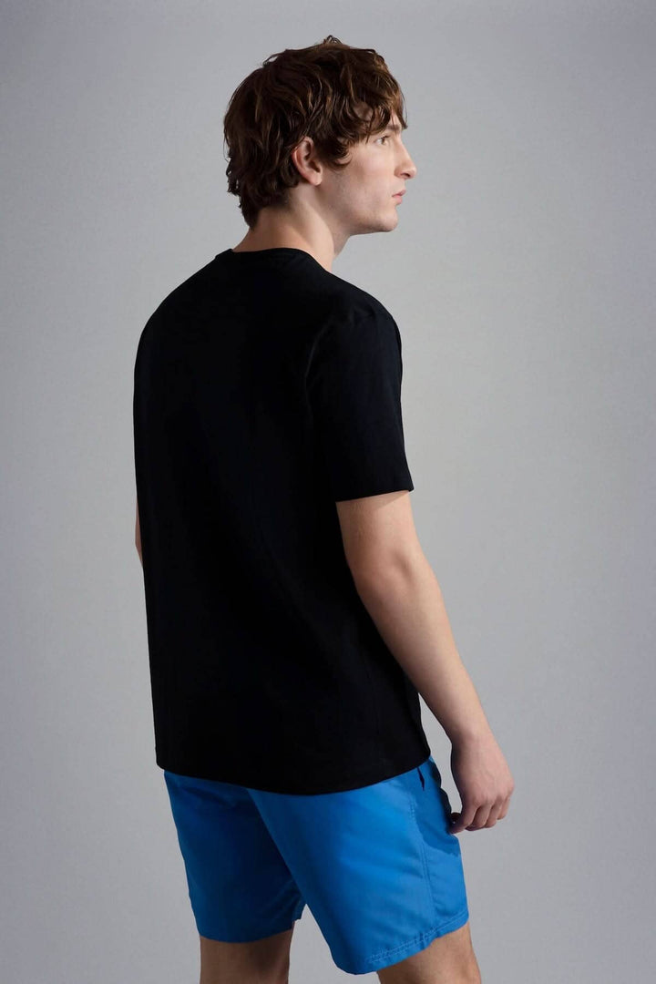 Homme portant un t-shirt noir avec un dos simple, associé à un short bleu.