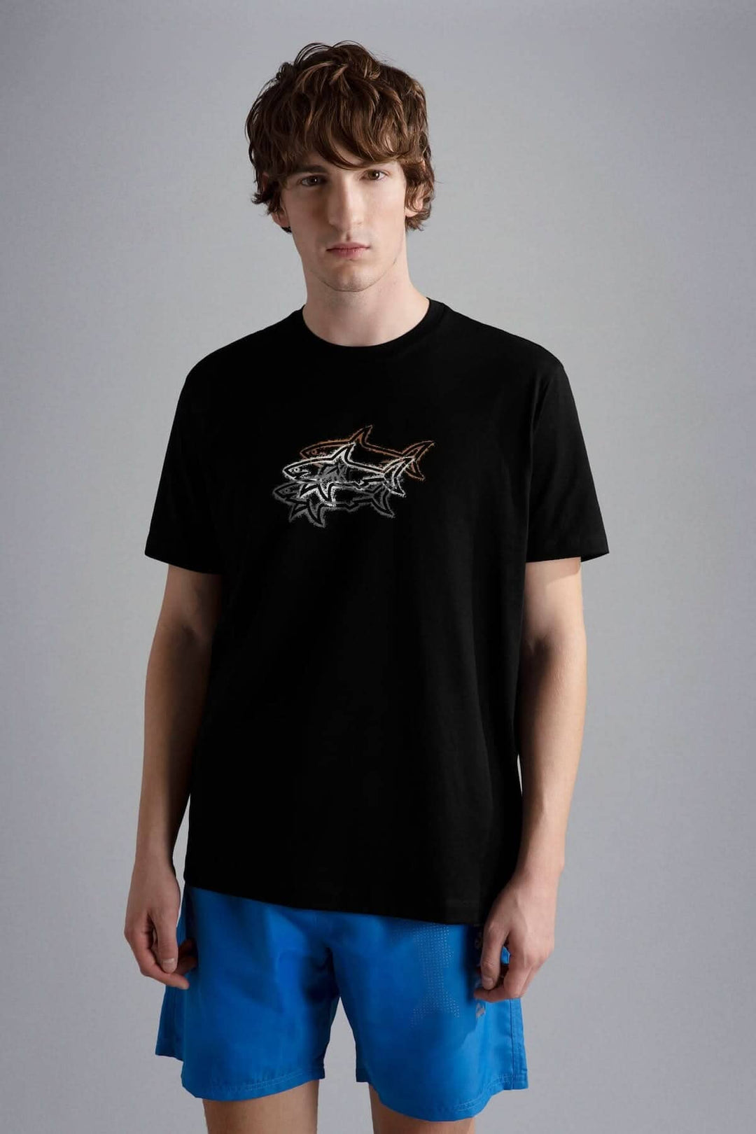 Homme portant un t-shirt noir avec un motif de 3 requins, associé à un short bleu.