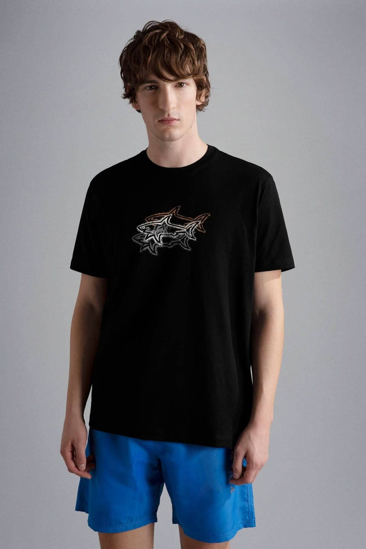 Homme portant un t-shirt noir avec un motif de 3 requins, associé à un short bleu.