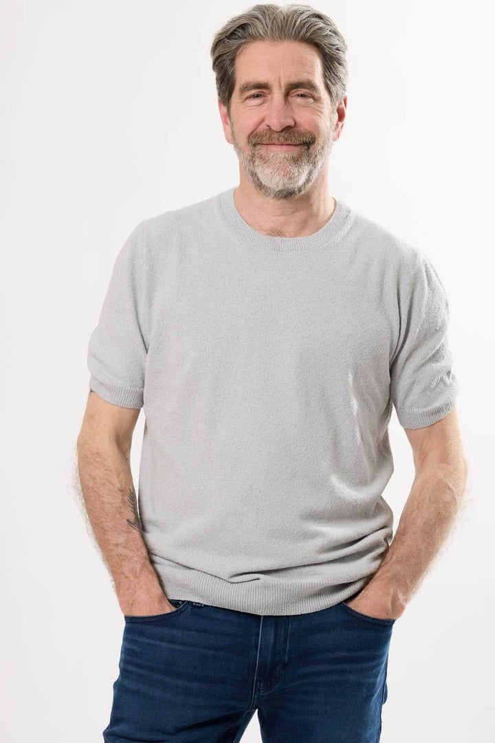 Homme souriant portant un t-shirt gris clair en coton, style décontracté, avec jeans.