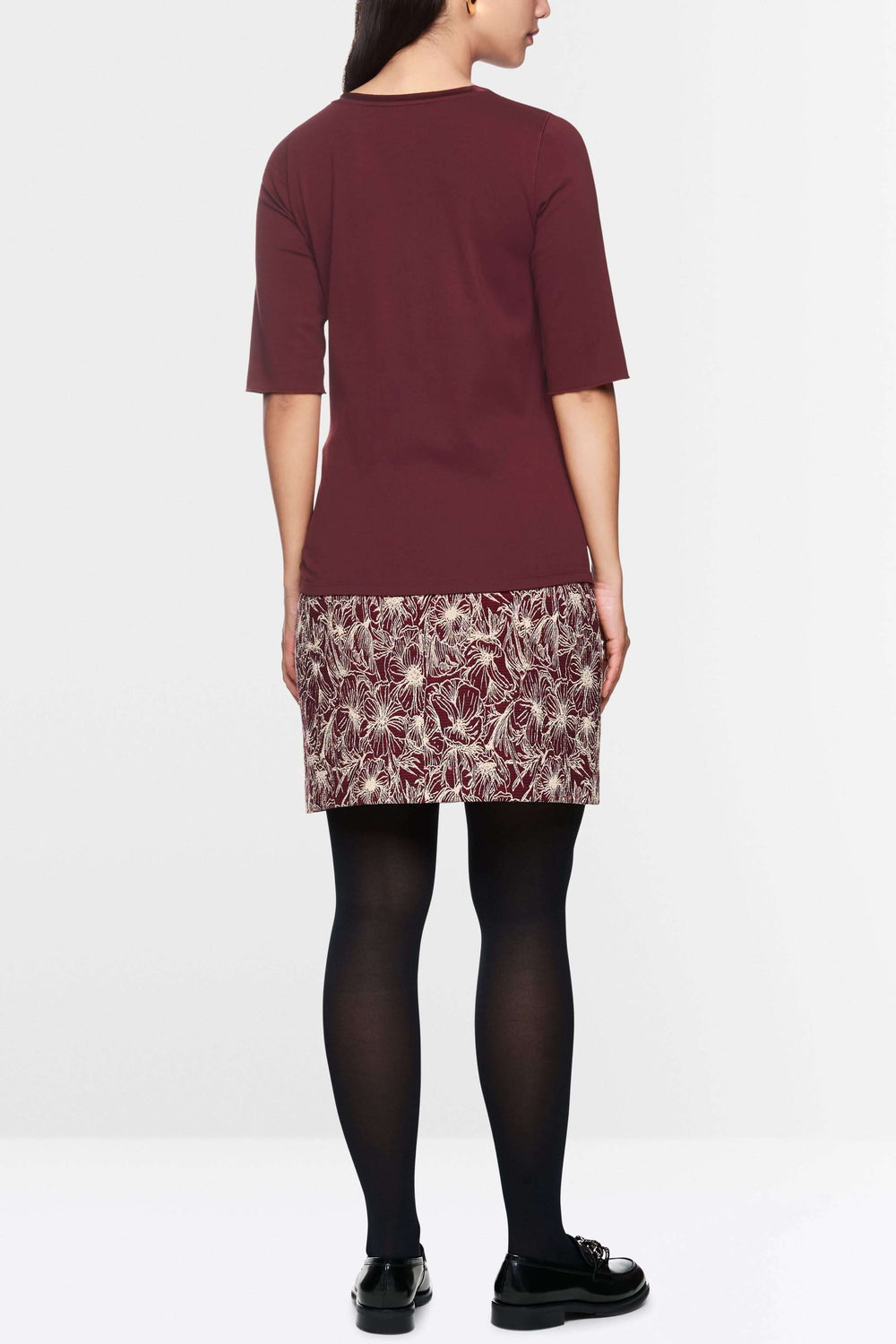 Femme vue de dos avec un t-shirt manches courtes et une jupe à motifs, style classique et élégant.