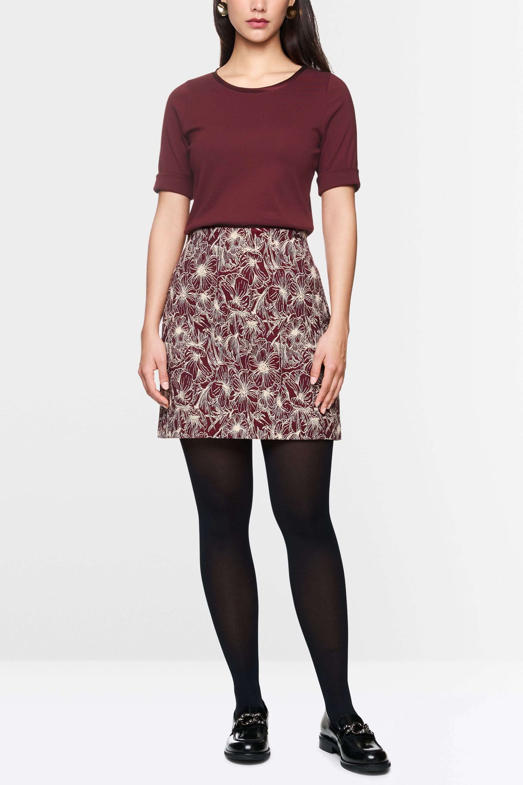 Femme portant un t-shirt manches courtes rouge et une jupe à motifs, look décontracté et élégant.