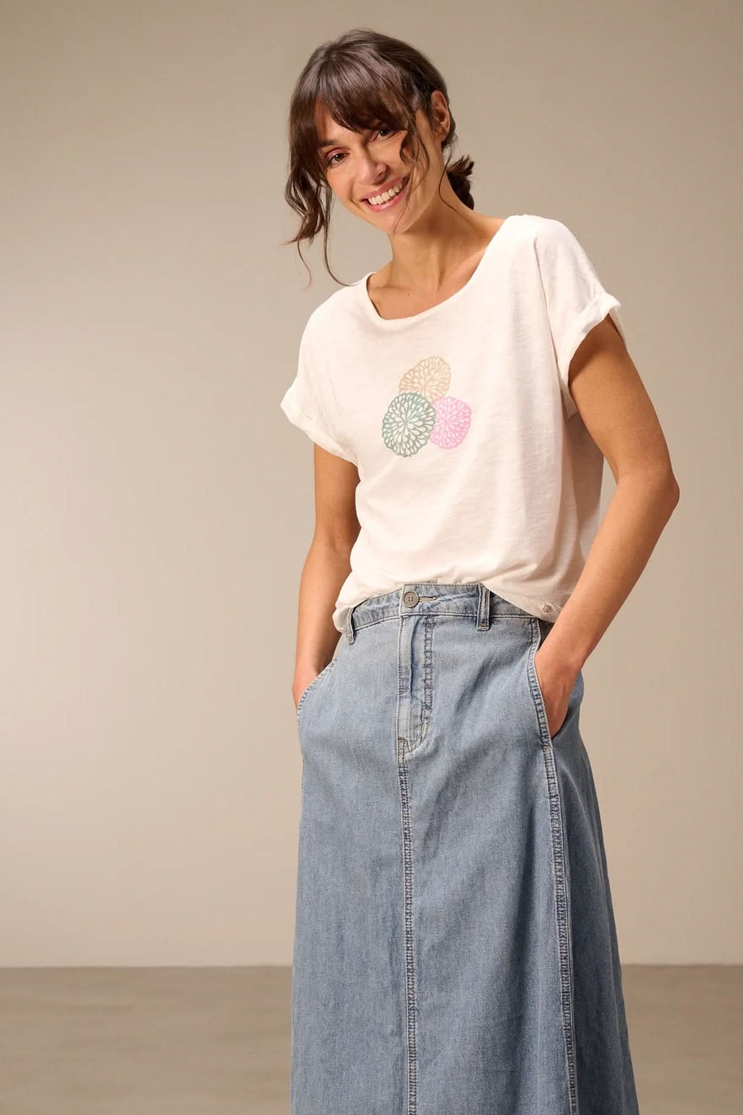 Femme portant un T-shirt à manches courtes coupe décontractée blanc avec un design graphique floral, jupe en jean décontractée.