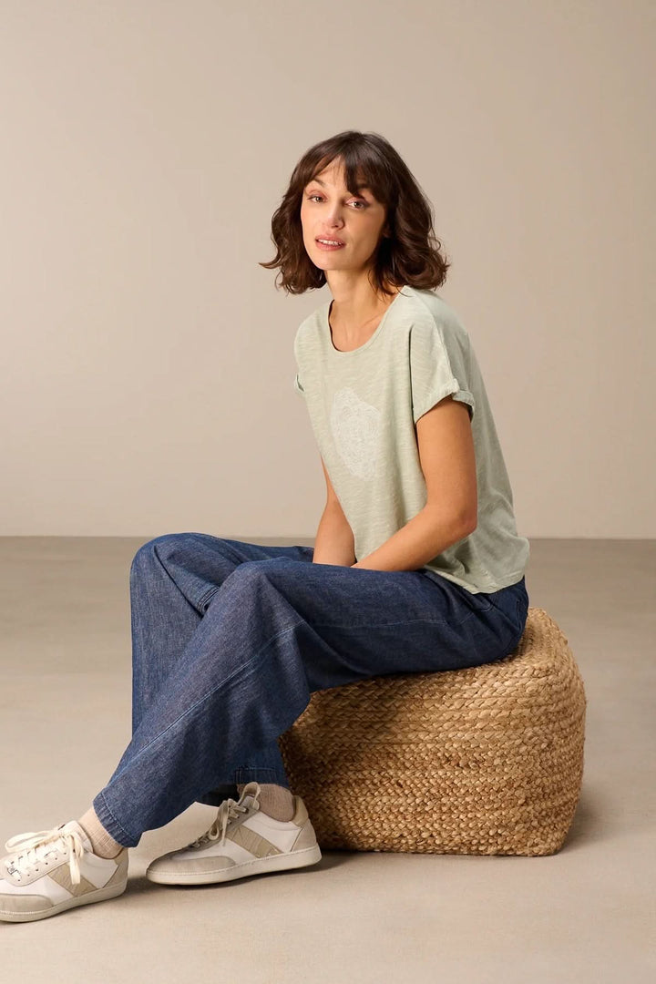 Femme portant un T-shirt à manches courtes coupe décontractée assise sur un pouf, style casual et confortable.