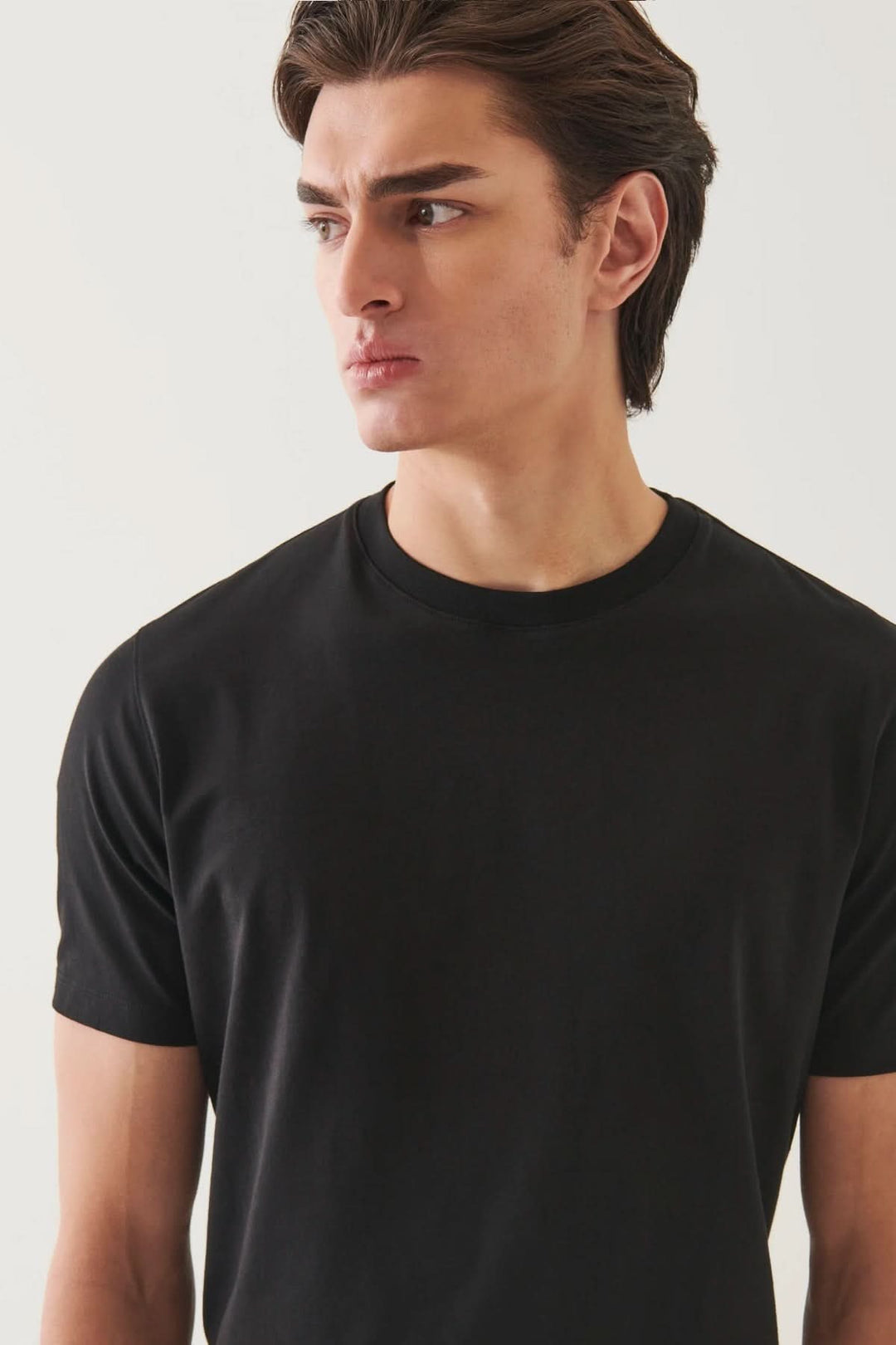 Homme portant un t-shirt minimaliste noir à col rond, offrant un style décontracté et élégant.