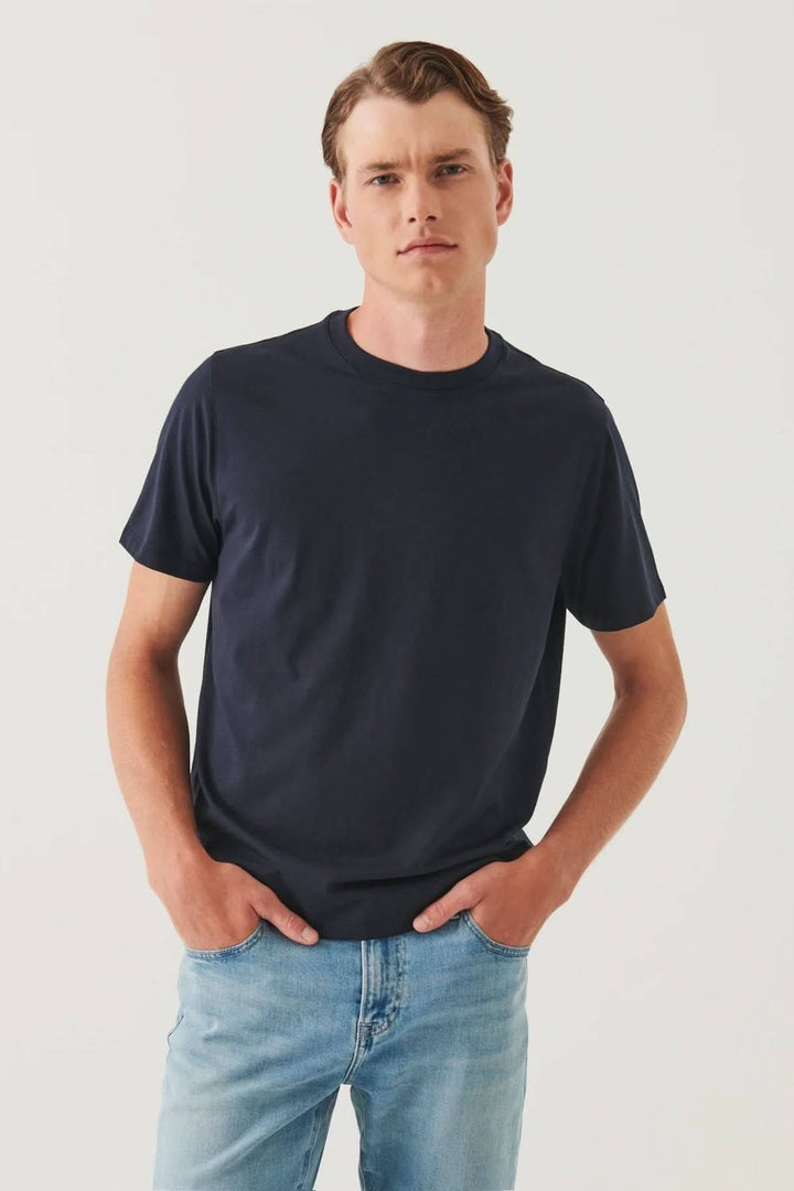 Homme portant un t-shirt minimaliste bleu marine, col rond et coupe droite, avec un look décontracté.