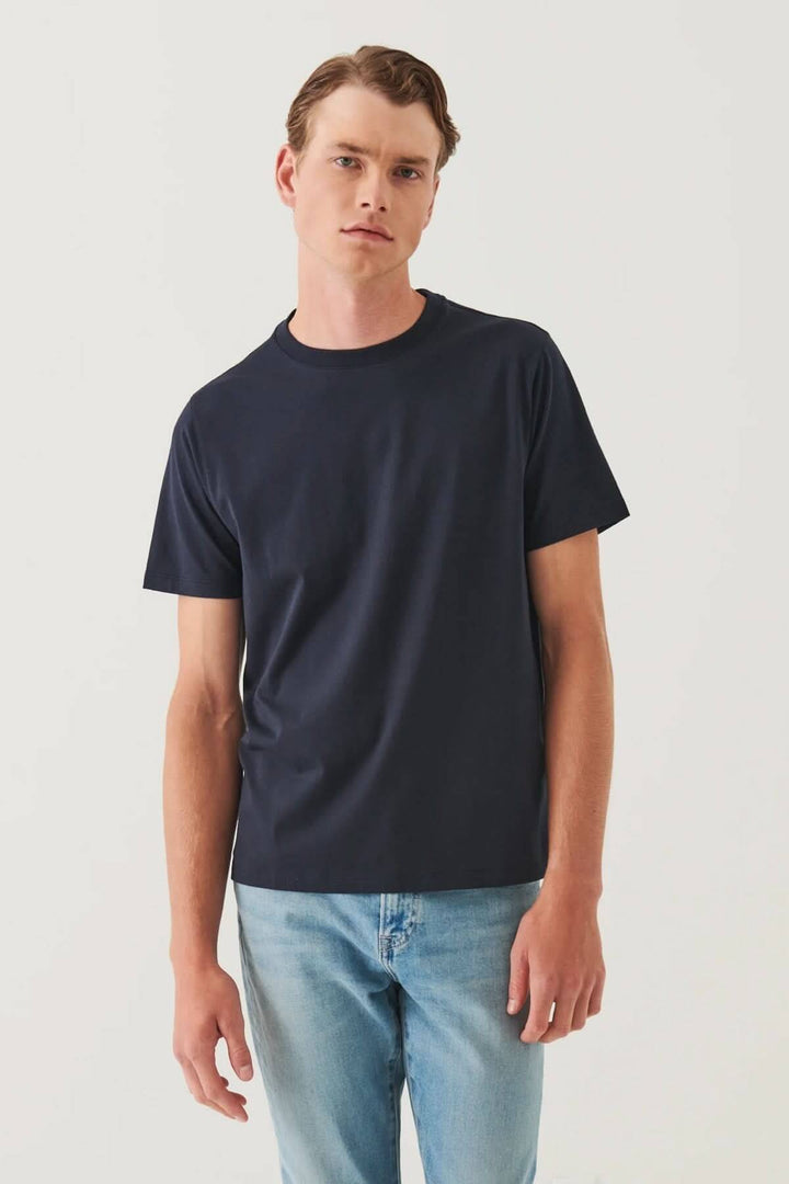 Homme portant un t-shirt minimaliste noir, col rond, coupe droite, associé à un jean léger.