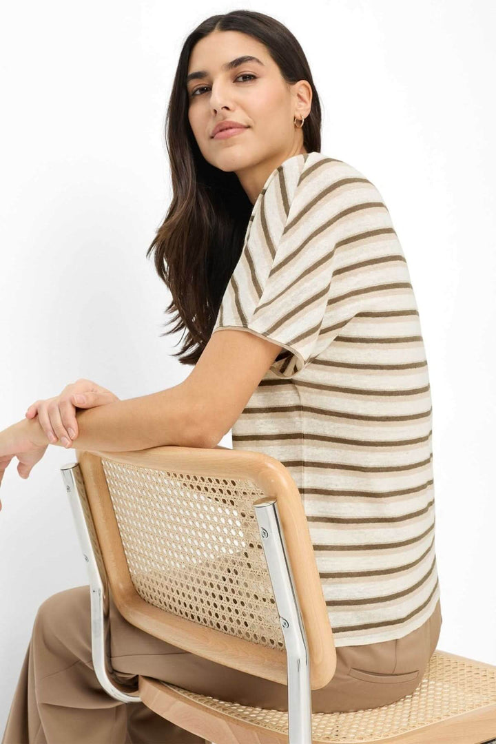Femme portant un T-shirt rayé CAELENS à manches courtes, motif à rayures horizontales, assise sur une chaise en rotin.