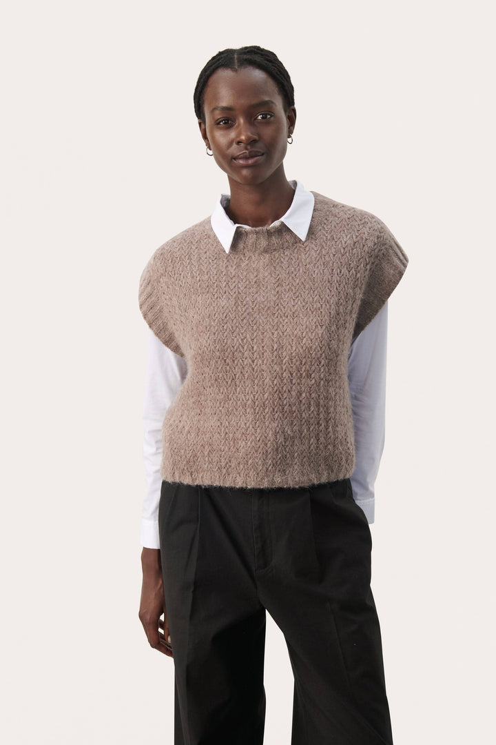 Tricot sans manches beige porté sur une chemise blanche, parfait pour les superpositions et le confort.