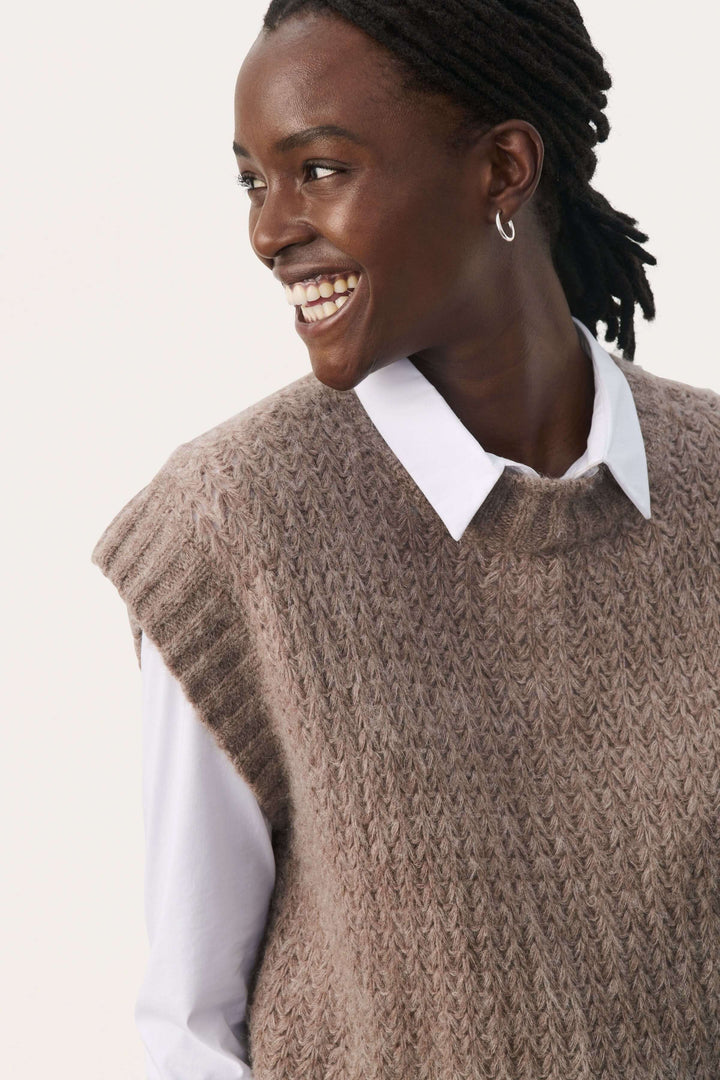 Femme souriante portant un tricot sans manches beige, parfait pour les superpositions, avec une chemise blanche.